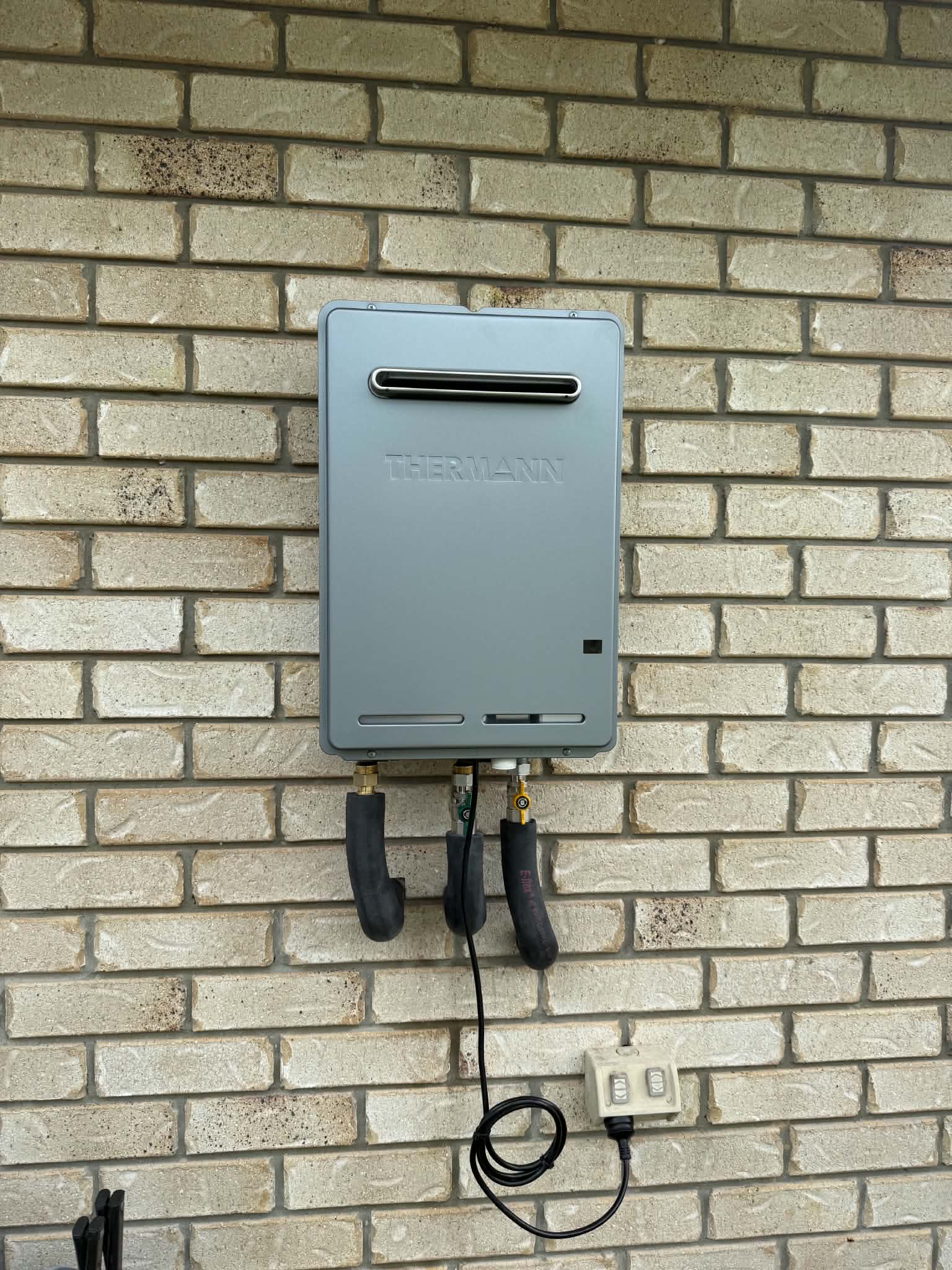 Thermann continuous flow gas hot water unit installed on a brick wall